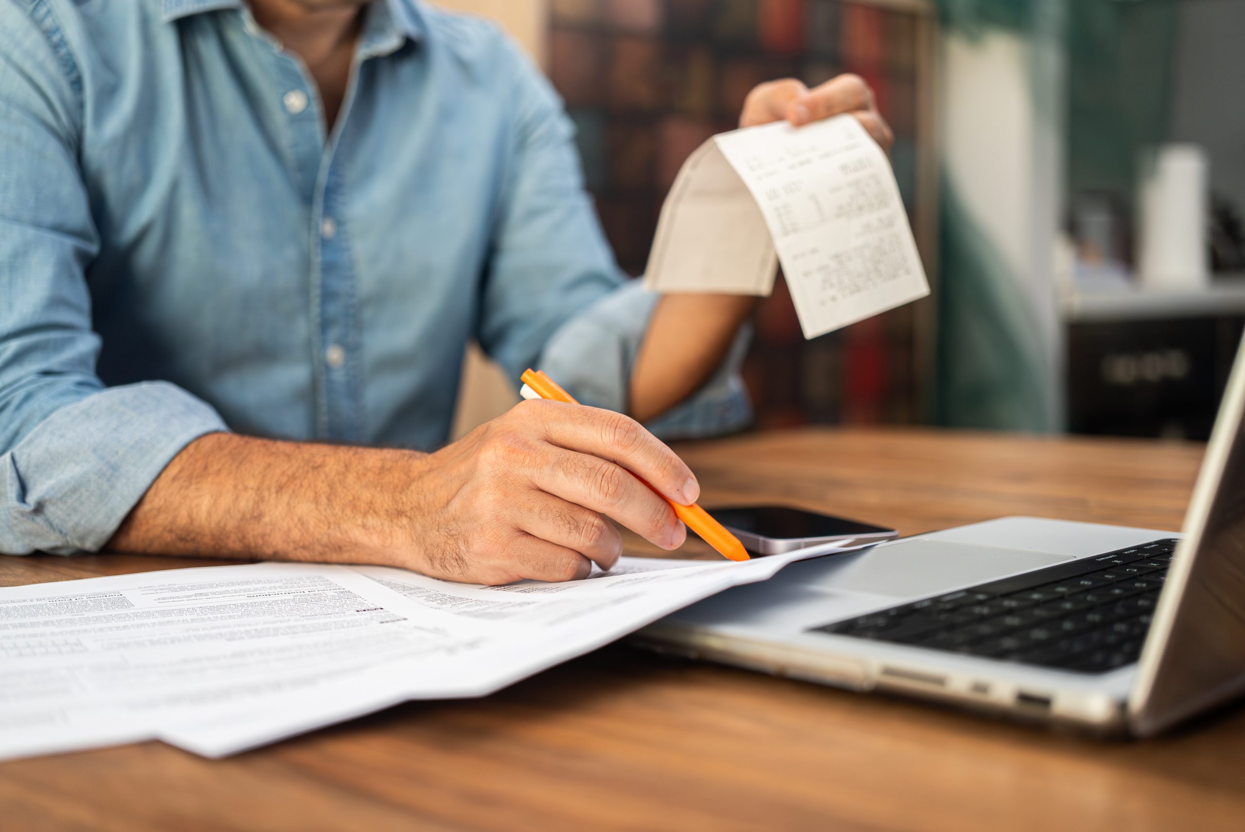 man filling out tax forms at home using a laptop and holding receipts. financial management and personal accounting concept during tax season.
